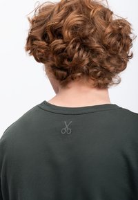 Donkergroen T-shirt met korte mouwen, ronde hals en een subtiele schaarafbeelding gedrukt op de achterste halslijn. Zacht materiaal, comfortabele pasvorm.