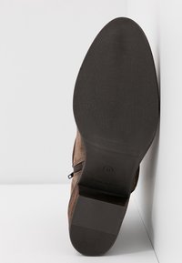 Botín de ante marrón con suela de goma negra texturizada, cuenta con una cremallera lateral, y está etiquetado con la talla 37, fabricado en España.