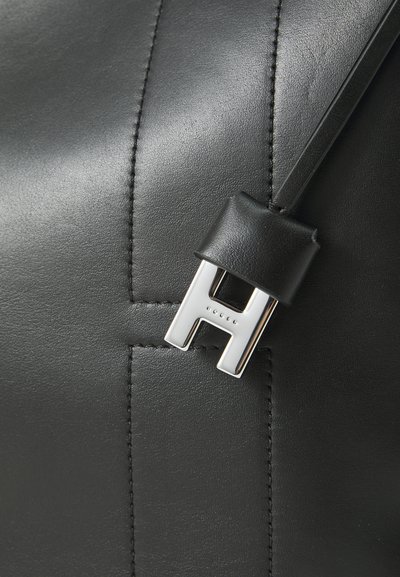 Geantă din piele neagră cu un accent distinct din metal argintiu în formă de 'H' și un textură netedă cu detalii de cusătură vizibile.