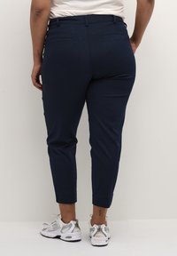 Navy blue tapered pants with stretch fabric, featuring back pockets, a smooth texture, and a cropped length, paired with white sneakers.