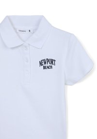 Polo bianca realizzata in cotone, caratterizzata da una texture a coste, un colletto classico, tre bottoni e il logo ricamato in nero "NEWPORT BEACH".