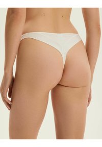Biały bawełniany thong, bezszwowy design, minimalne krycie, gładka faktura, z paskiem o średnim wzroście i bez widocznych elementów metalowych.