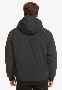 Black, padded jacket with a hood, featuring elastic cuffs and a relaxed fit. Fabric has a smooth texture and sturdy seams.