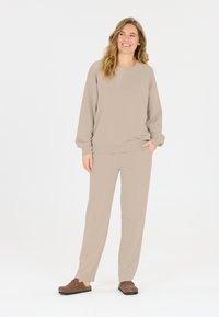 Hoodie beige dan celana matching terbuat dari kain lembut; bentuk santai dengan manset dan pinggang rajut; dipadukan dengan klompen coklat. Desain yang sederhana.