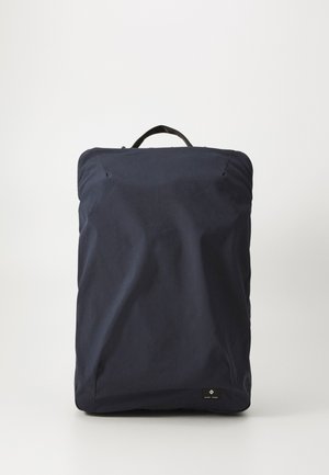 Rucsac albastru închis cu țesătură texturată, formă rectangulară, mâner superior și o etichetă mică neagră în partea de jos. Design minimalist.