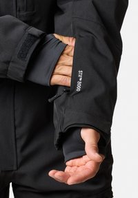 Zwarte prestatiek jacket met klittenbandmanchetten en een duimgat aan de binnenzijde. Heeft STYX™ 8000 branding en een verstelbare ritszak op de mouw.