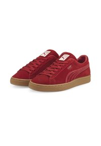 Zapatillas de ante rojo con suela de goma, que presentan costuras blancas y etiquetas de logo prominentes en la lengüeta. Diseño de perfil bajo con cordones.
