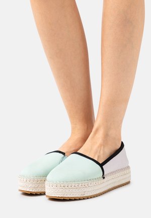 Espadrilles en toile vert clair avec garnitures noires, semelle intermédiaire en jute tressé et semelle extérieure en caoutchouc texturé. Bout rond et design facile à enfiler.