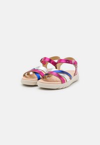 Sandales multicolores avec des brides brillantes rose, argent et bleu, design ouvert à l'avant, et semelle beige texturée ; bride réglable à la cheville.