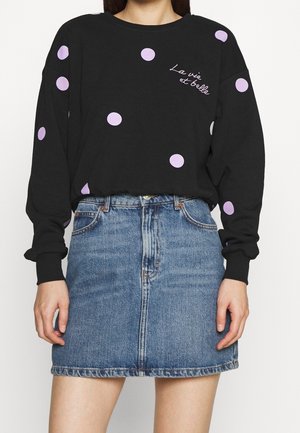 Zwarte top met lange mouwen met lavendelkleurige polkadots en tekst "La vie est belle", gecombineerd met een blauwe denim minirok.