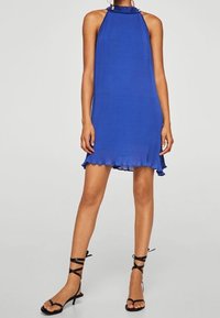 Robe bleue à col halter avec une texture côtelée et un ourlet volanté, assortie à des sandales noires à lanières. Design minimaliste, longueur mi-cuisse.