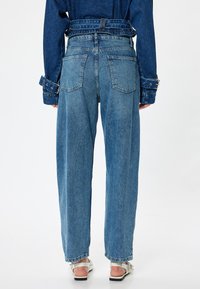 Jeans de mezclilla azul claro, de tiro alto y con un corte holgado. Cuenta con cuatro bolsillos, pasadores para cinturón y dobladillos remangados. Textura suave con detalles desgastados.