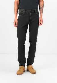 Zwarte denim jeans met een rechte pasvorm, vijf-pocket ontwerp, subtiele wassing en contrasterende stiksels, gecombineerd met tan sneakers.