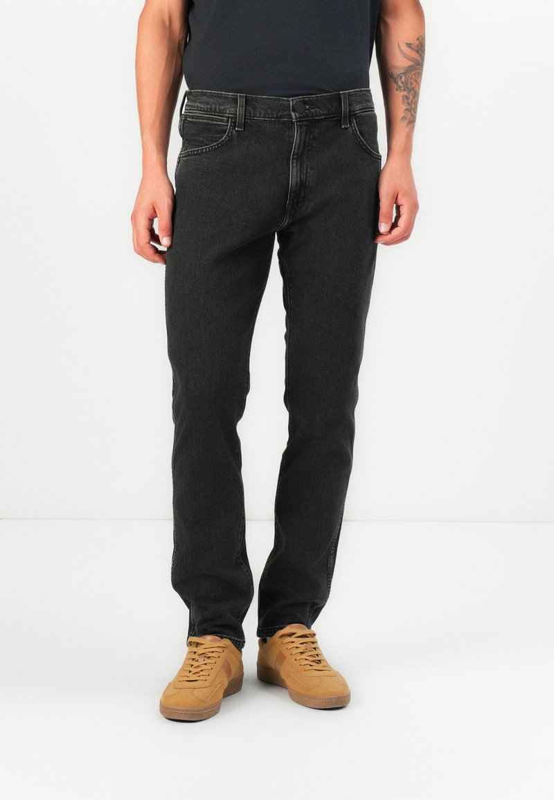 Zwarte denim jeans met een rechte pasvorm, vijf-pocket ontwerp, subtiele wassing en contrasterende stiksels, gecombineerd met tan sneakers.