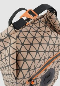 Waterdichte rugzak met een geometrisch patroon in beige en zwart, met een oranje rits en een stevige zwarte draagriem.