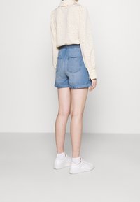 Farkkushortsit, joissa on revitty helma, vaaleansininen väri, kaksi takataskua, yhdistettynä pilkulliseen puseroon ja valkoisiin tennareihin.