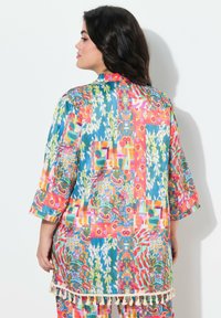 Copertura in stile kimono colorata e ritmata con maniche tre quarti, caratterizzata da un mix di fiori e design geometrici. Rifinita con frange all'orlo.