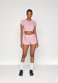 Roosa sportlik lühike top ja sobivad lühikesed püksid, millel on sile tekstuur ja valge Nike logo. Modell kannab musti spordijalatsid ja valgeid sokke.