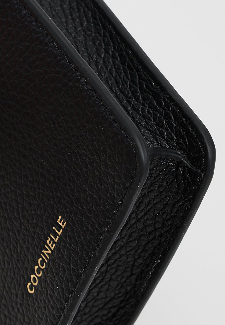Schwarze, strukturiert Lederhandtasche mit glatten Kanten, versehen mit einem dezenten goldenen Logo "Coccinelle" auf der Vorderseite. Akzente betonen ihr strukturiertes Design.