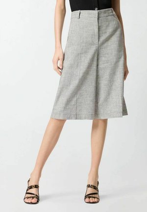 Femme portant une jupe gris clair au genou avec un pli avant, un haut noir sans manches et des sandales noires à talons hauts à brides.