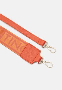 Cinghia arancione con spalline in pelle testurizzata e una larga sezione in tessuto con lettering audace. Include attacchi in metallo per il fissaggio.
