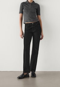 Czarne dżinsy z wysokim stanem zestawione z szarą prążkowaną koszulką polo z suwakiem przy kołnierzu. Model nosi czarne mokasyny. Gładka faktura, dopasowany krój.