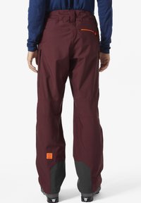 Bordeaux ski broek met een rechte snit, verstevigde zwarte onderbenen en een oranje accentzak. Gemaakt van waterafstotend materiaal.