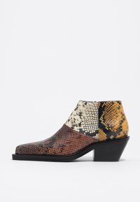 Botín con parte superior de patrón de serpiente multicolor en tonos marrón, beige y amarillo, con punta afilada y tacón bajo negro.