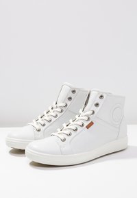 Weiße High-Top-Sneaker aus glattem Leder mit Metall-Ösen, flachen Schnürsenkeln und einem Logo-Akzent an der Seite. Gerundete Gummisohle.