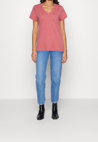 Lyserød bomulds t-shirt med V-hals-design, korte ærmer og glat tekstur, parret med blå lige ben jeans og sorte ankelstøvler.