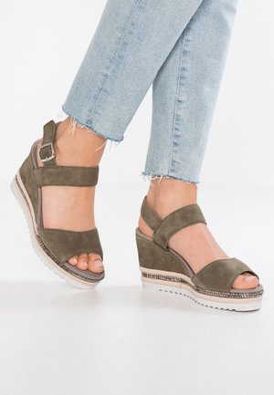 Sandales compensées en suede vert olive avec orteil ouvert, bride de cheville réglable et semelle blanche texturée ; accent tissé contrastant autour de la base.