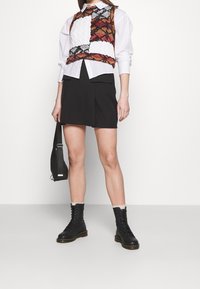 Neulemekko monivärisenä, valkoisen paidan päällä, yhdistetty mustan minihameen ja mustien nauhakenkien kanssa, joissa on paksu pohja.