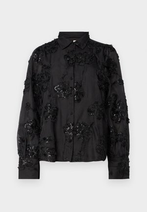 Mustapaitahihanshirt, jossa on kukka- ja paljettikirjontaa, pitkät hihat, pehmeä pinta ja klassinen kaulustyyli. Koristeltu kohotetuin kuvioin.