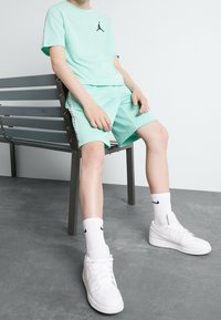 Tyrkysové tričko Jordan s černým logem, doplněné o shodné tyrkysové síťované kraťasy. Bílé tenisky Nike a jemné bílé ponožky.