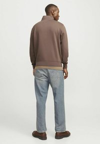 Ruskihi yüksek yakalı sweatshirt, ribana kollar ve alt kısmıyla, açık mavi kot pantolon ve kahverengi ayakkabılarla eşleştirilmiş, temiz ve günlük bir arka görünüm sergiliyor.