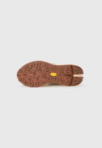 Semelle de chaussure en caoutchouc marron avec un motif de grip texturé, comportant une section beige et un logo circulaire jaune au centre.