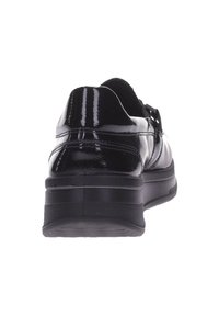 Zapato de charol negro visto desde el talón, con una suela gruesa y costuras visibles alrededor de la parte posterior.