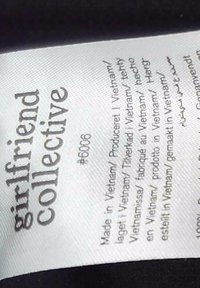Girlfriend Collective mærke med produktnummer #6006 og produktionsoplysninger med angivelse af fremstillet i Vietnam på flere sprog på en hvid stofetiket.