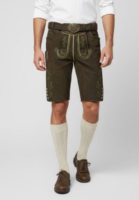 Pantaloni corti in pelle marrone con ricami verdi, tasche laterali e bottoni decorativi. Indossati con calze color crema fino al ginocchio e scarpe marroni.