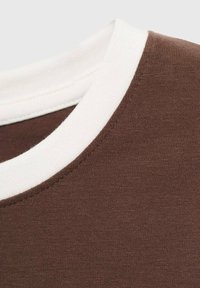 Rjav t-shirt z izrezom, ki ima kontrastno belo rebrasto obrobo. Mehka tekstura blaga s gladkim zaključkom. Posnetek podrobnosti v povečavi.