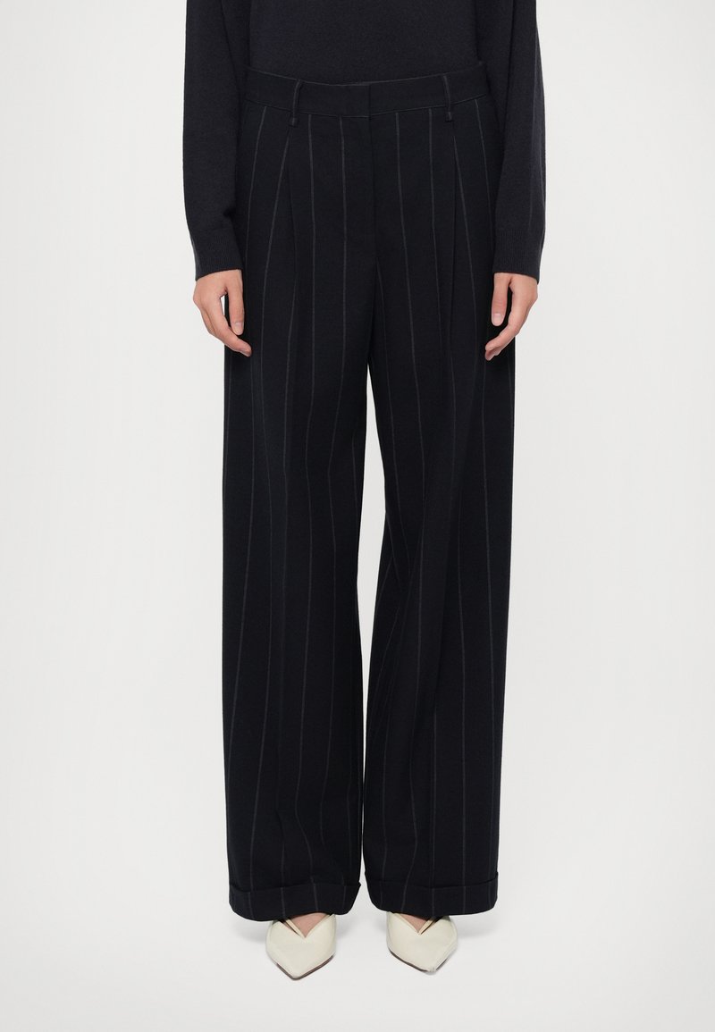 Pantaloni neri a gamba larga con righe verticali bianche, realizzati in tessuto morbido, presentano una vita sagomata e un orlo a risvolto.
