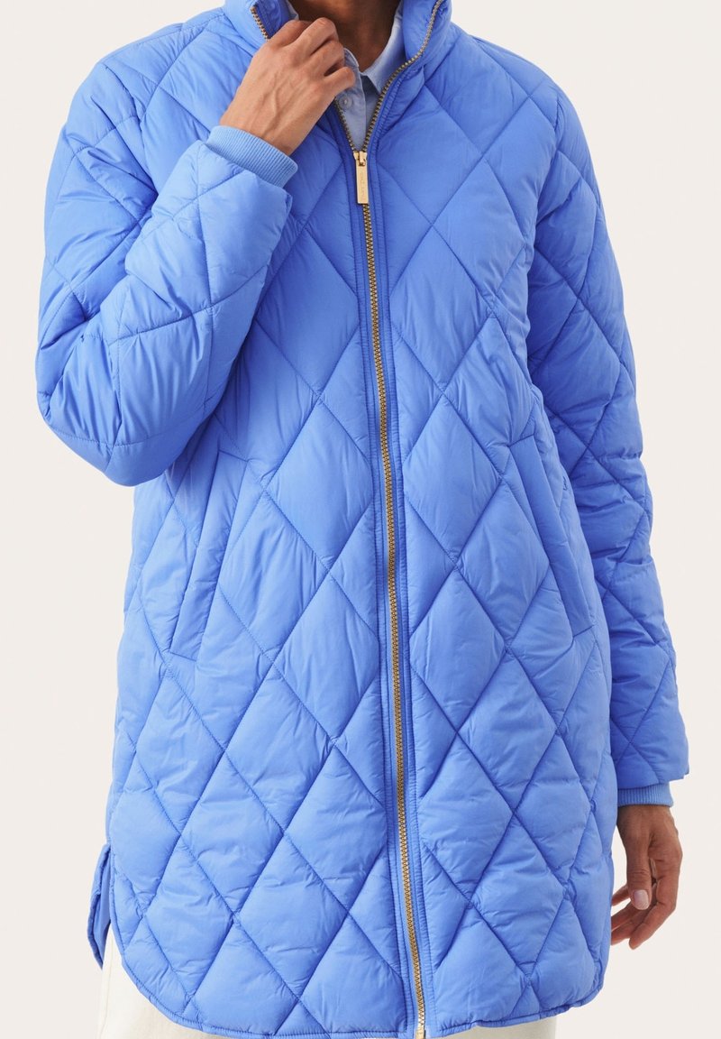 Niebieska pikowana kurtka z wysokim kołnierzem, zapięciem na zamek i prążkowanymi mankietami. Posiada wzór w diamenty oraz boczne rozcięcia dla swobody ruchów.