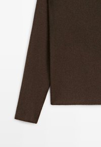 Maglione lavorato a maglia marrone a maniche lunghe, con manica e parte del torso su sfondo bianco, che mostrano la texture del tessuto e l'orlo dritto.