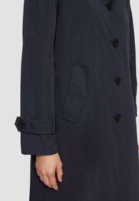 Marineblauwe jas met knoopsluiting aan de voorkant, zijzakken en verstelbare mouwen met knoopdetails. Glad materiaal en getailleerde pasvorm.