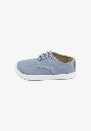 Zapato casual de lona azul claro con suela blanca y cordones a rayas azules y blancas, mostrado de perfil sobre fondo blanco.