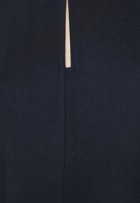 Nahaufnahme eines dunkelblauen Stoffes mit einem vertikalen Schlitz, der einen schmalen Streifen heller Haut darunter zeigt.