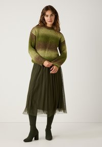 Gebreide trui in groen en bruine ombre; geplooide olijfgroene rok met doorschijnende overlay; bijpassende groene kniekousen en schoenen met blokhak.