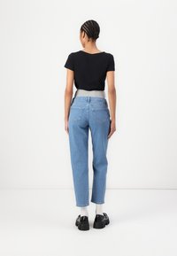 Una maglietta nera a maniche corte abbinata a jeans in denim azzurro chiaro con una vita grigia e tasche posteriori. Scarpe nere chunky completano il look.
