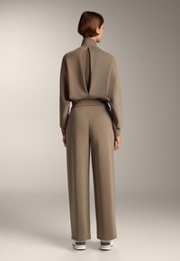 Koordinovaný dvojdielny outfit z textúrovaného taupe materiálu. Vybavený vysokým golierom a detailom otvoreného chrbta na vrchu, doplnený širokými nohavicami.