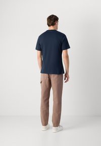 Ναυτικό βαμβακερό μπλουζάκι με κοντά μανίκια, όψη από πίσω, συνδυασμένο με ανοιχτό καφέ παντελόνι και λευκά παπούτσια. Απλός σχεδιασμός, χωρίς ορατά μοτίβα ή ακκαέντες.